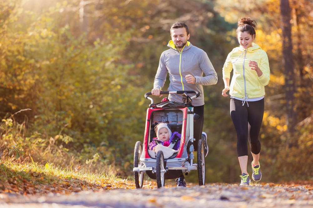 family with a father and a mother and a baby in a stroller outside running on a fall day
